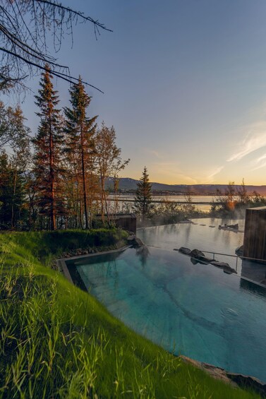 A clear swimming pool surrounded by trees and a view of a lake and mountains. 5