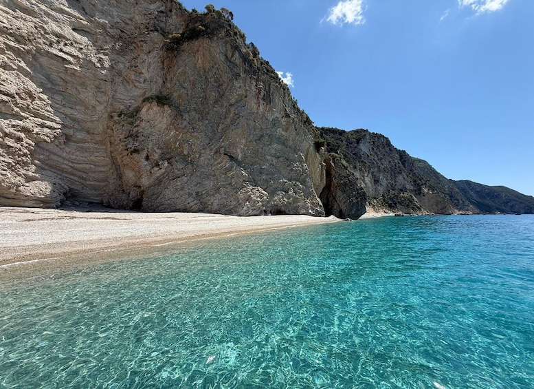 A clear turquoise sea, a sandy beach, and rocky cliffs. 1