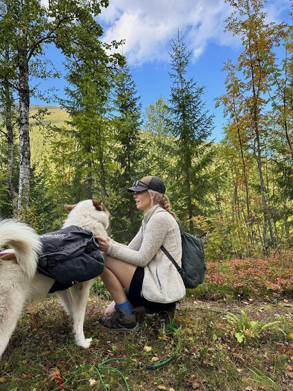 A person in a forest with a dog, wearing a cap and carrying a backpack. 3