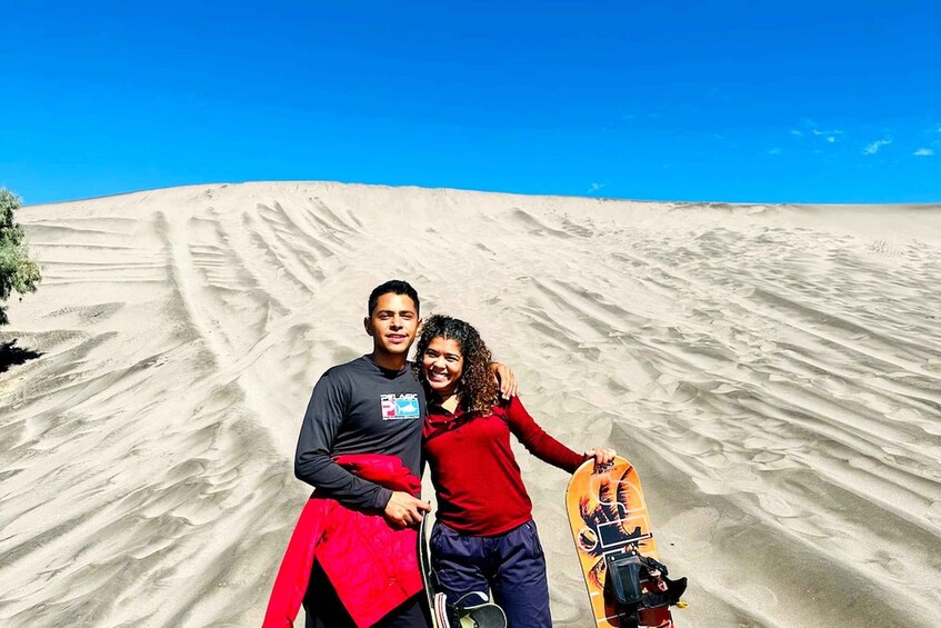 Two people standing in a desert with sand dunes in the background. 3