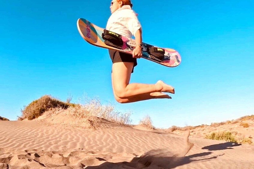 A person mid-jump with a snowboard, desert landscape, and clear sky. 4