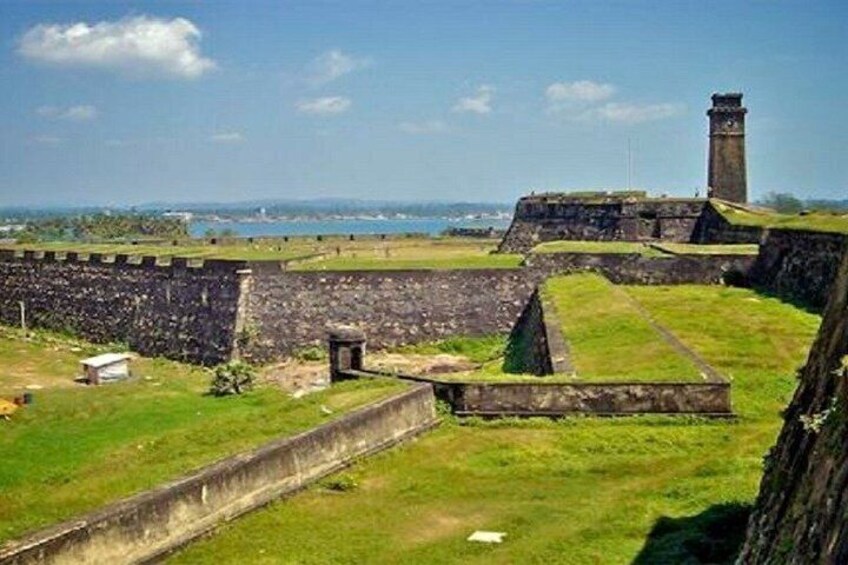 A coastal fortification with a lighthouse, stone walls, and grassy terrain. 4