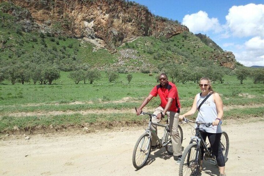 Deux personnes à vélo dans un paysage rural, avec un chemin de terre et une végétation verdoyante. 1