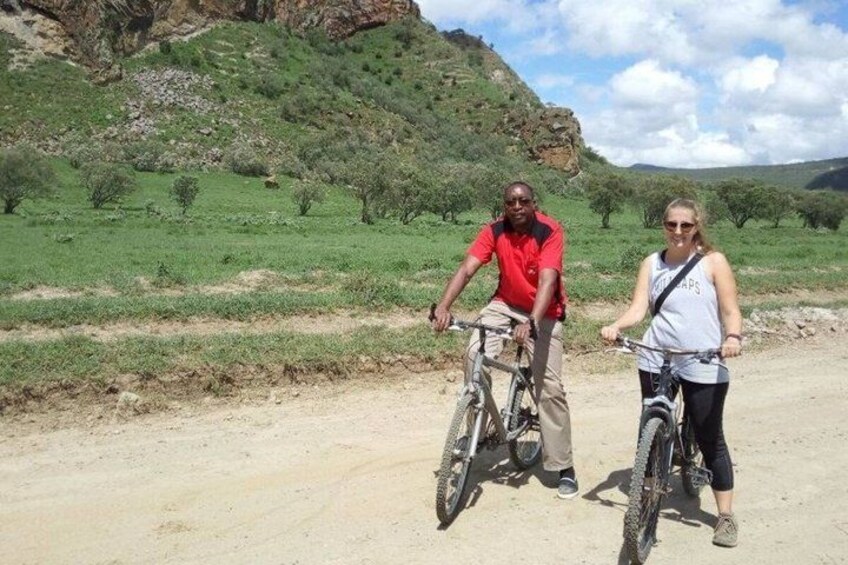 Deux personnes à vélo dans un paysage rural, avec un chemin de terre et des champs verdoyants. 4