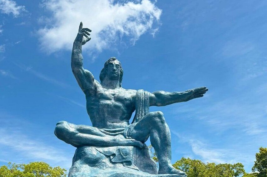 A bronze statue of a seated man with one arm raised, set against a clear blue sky. 1