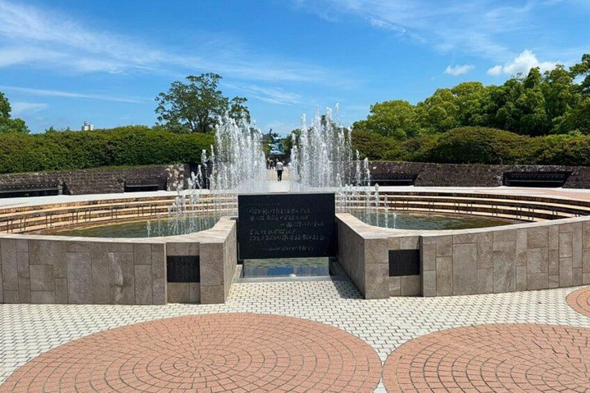 A fountain with water jets, a paved walkway, and a plaque with text. 4