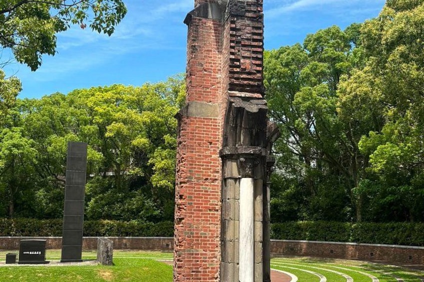 A brick monument with a metal plaque, surrounded by lush green trees and a clear sky. 3