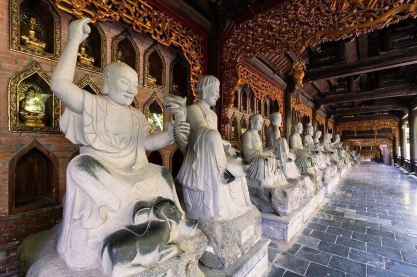 A row of seated stone statues in a corridor with ornate golden decorations and brick walls. 2