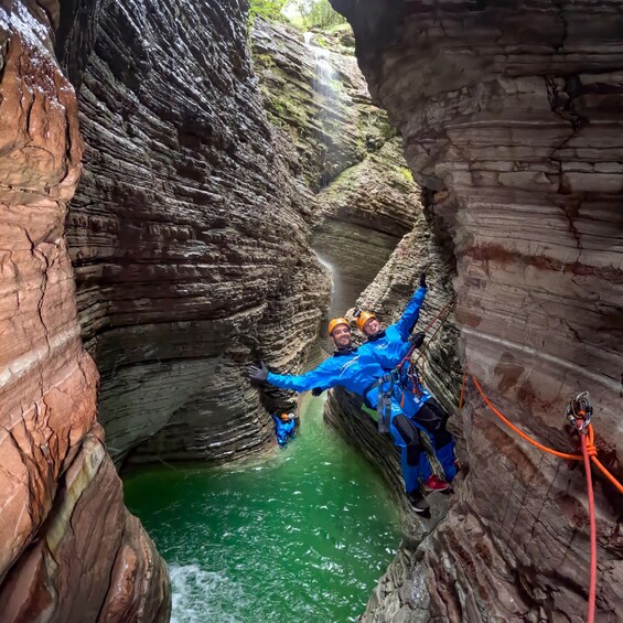 Two people rappelling down a rocky canyon with a river below. 3