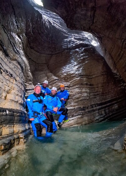 A group of people in blue diving suits sitting in a narrow, rocky water channel. 4