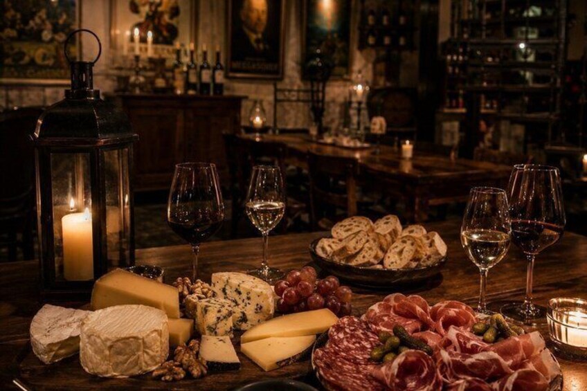 A charcuterie board with cheese, meats, and grapes, accompanied by wine glasses and a lit candle, set in a dimly lit room with wooden furniture and a vintage ambiance. 4