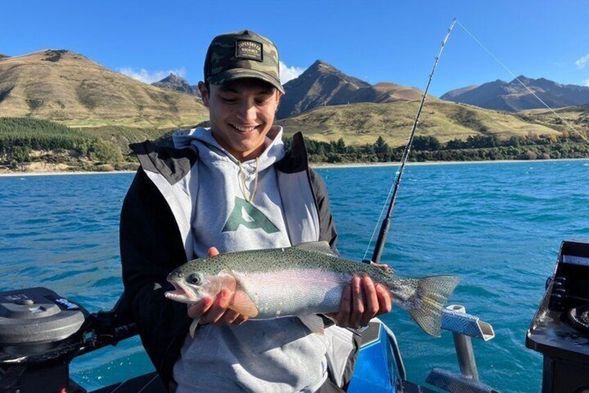 A person holding a fish on a boat with a mountainous landscape in the background. 5
