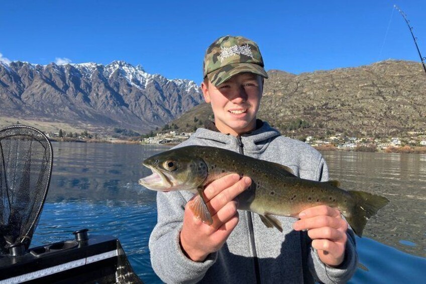 A person holding a fish by a lake with mountains in the background. 1