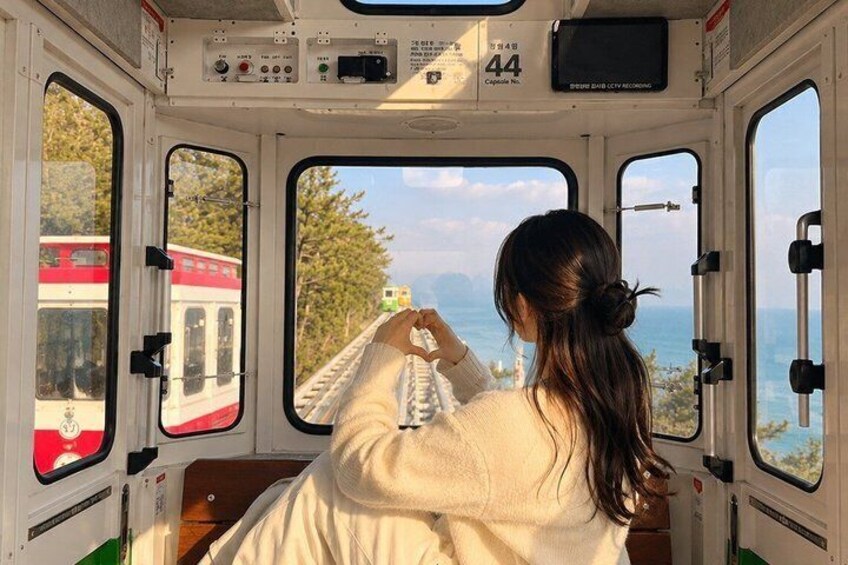 A train interior with a passenger holding a camera, a train window, and a view of another train outside. 1