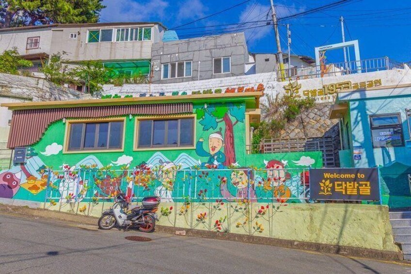 A colorful building with a mural, a motorcycle parked in front, and a sign that says 'Welcome to Daebang-dong.' 5