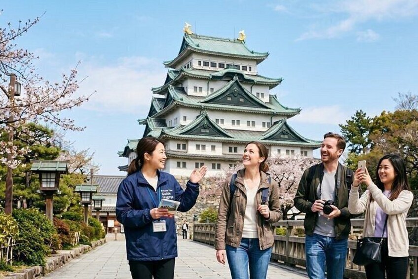 Un grupo de personas frente a un castillo japonés tradicional, rodeado de flores de cerezo. 1