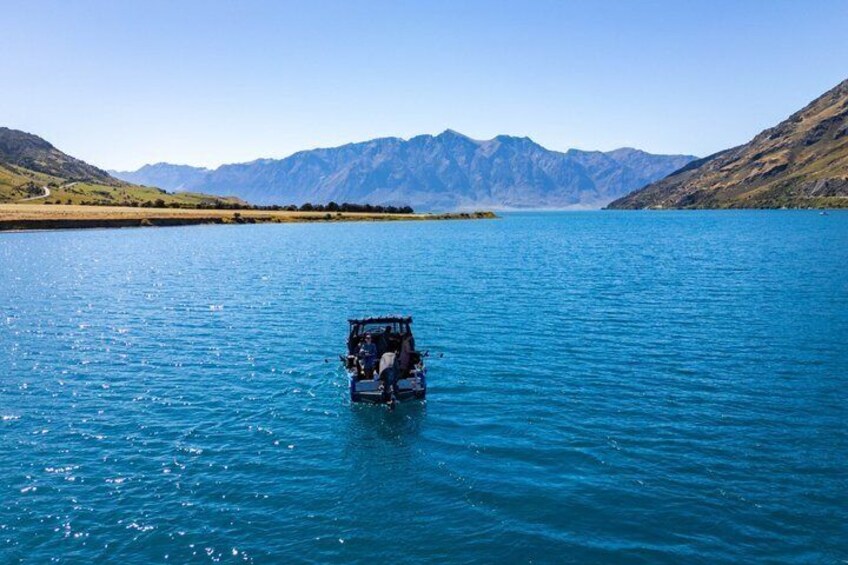 A vehicle on a calm lake with mountains in the background. 2
