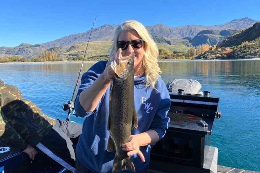 A person holding a fish on a boat with mountains in the background. 1