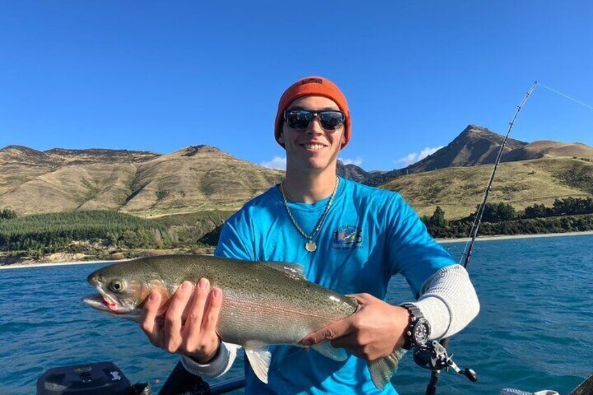 A person holding a fish on a boat with a mountainous landscape in the background. 3