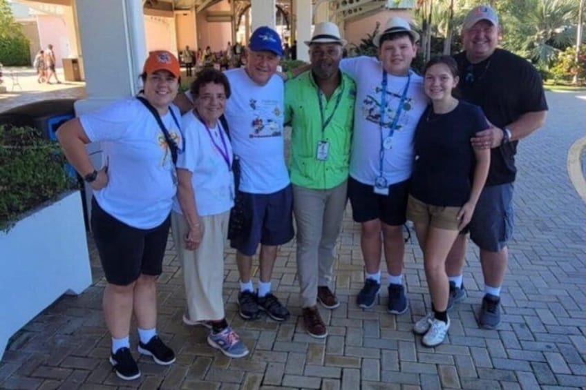 A group of people standing on a paved walkway, some wearing lanyards and casual clothing. 1