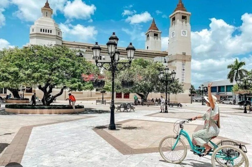 A person riding a turquoise bicycle in a plaza with a historic building in the background. 5