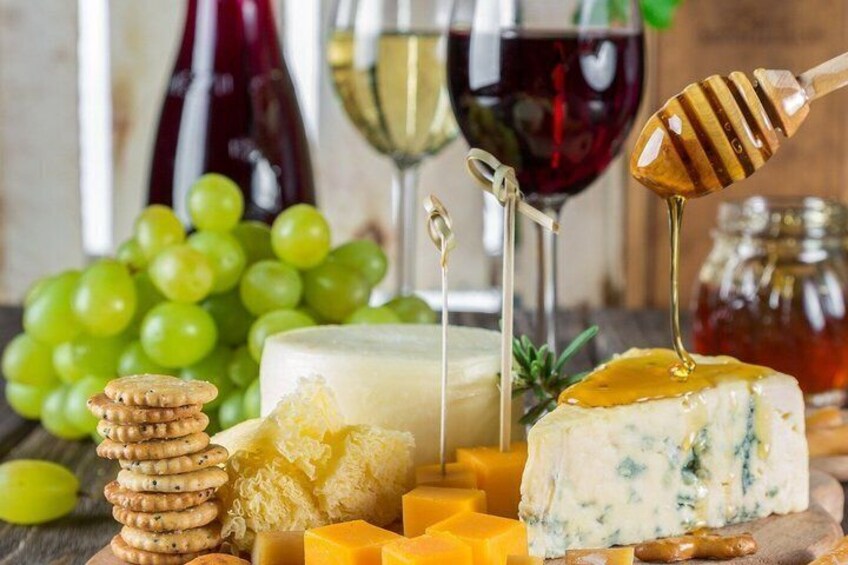 A variety of cheeses, crackers, grapes, and honeycomb with a wine glass and bottles in the background. 2