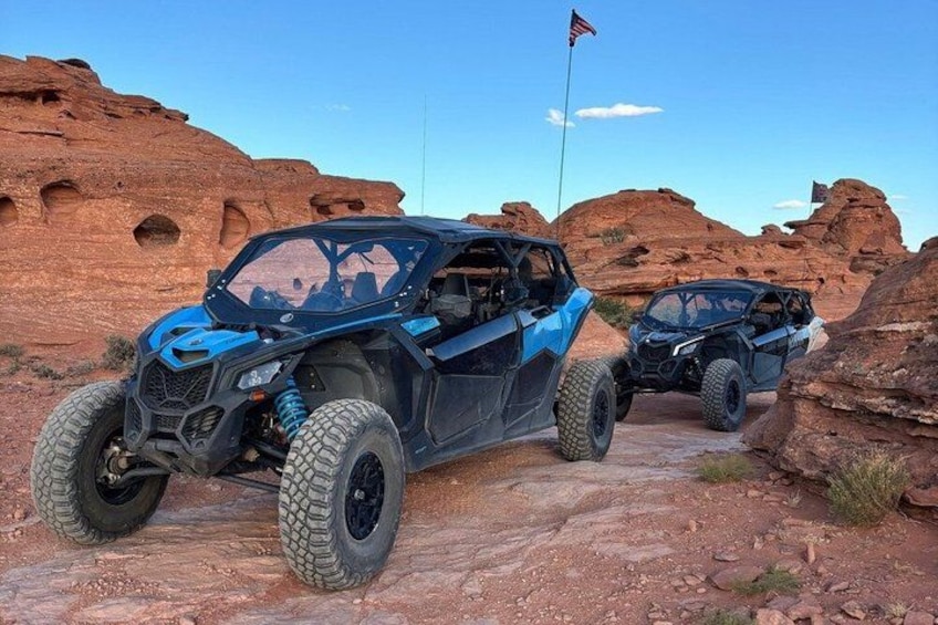 Two off-road vehicles parked on a rocky terrain with red rock formations in the background. 4