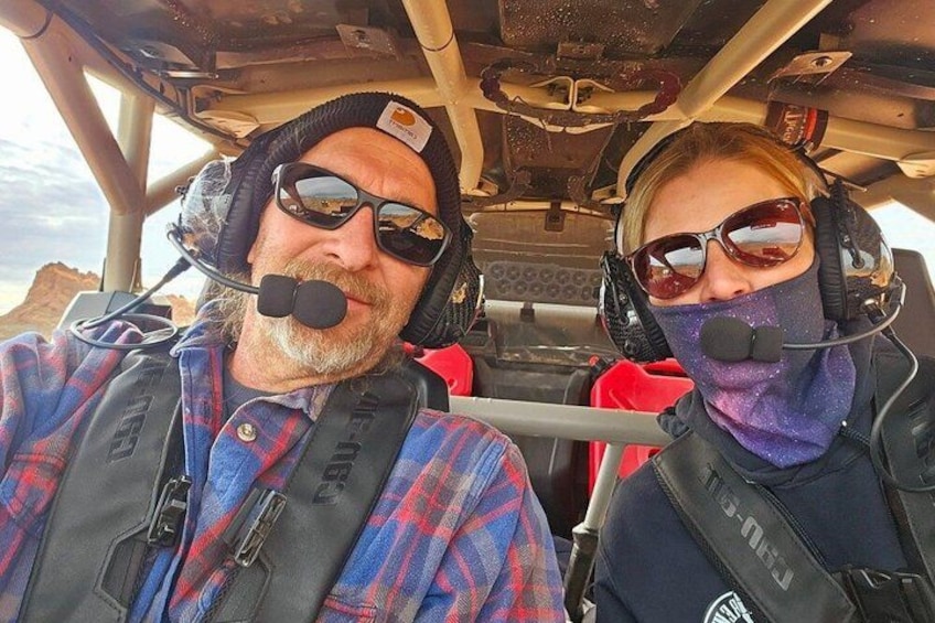 Two people in a vehicle with a rugged interior, wearing headsets and safety vests. 2