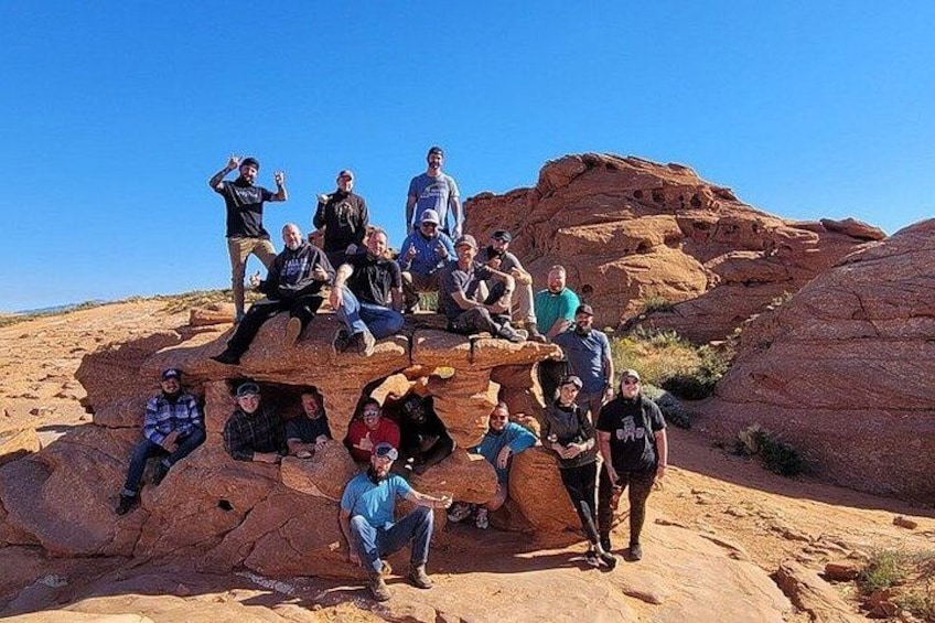 A group of people posing on a rocky outcrop with a clear blue sky in the background. 1
