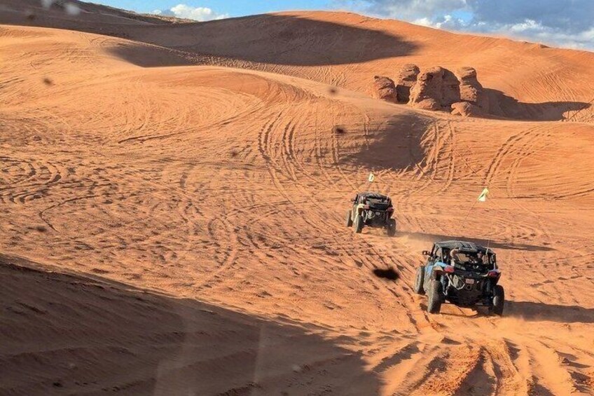 Two off-road vehicles on a sandy desert landscape with undulating terrain and rock formations. 3