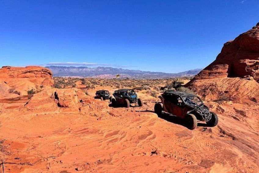 Off-road vehicles in a desert landscape with red rock formations and a clear blue sky. 4