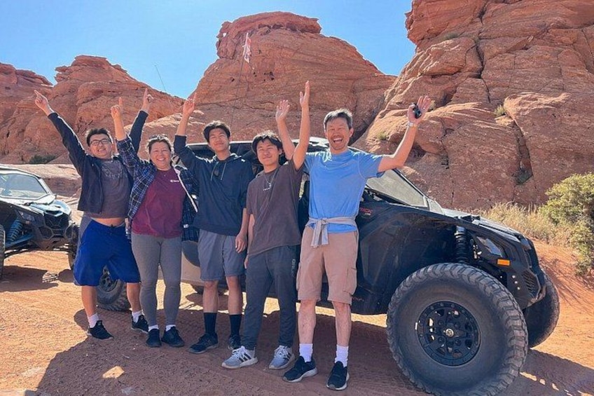 A group of people posing with a black off-road vehicle in a desert landscape with red rock formations. 1