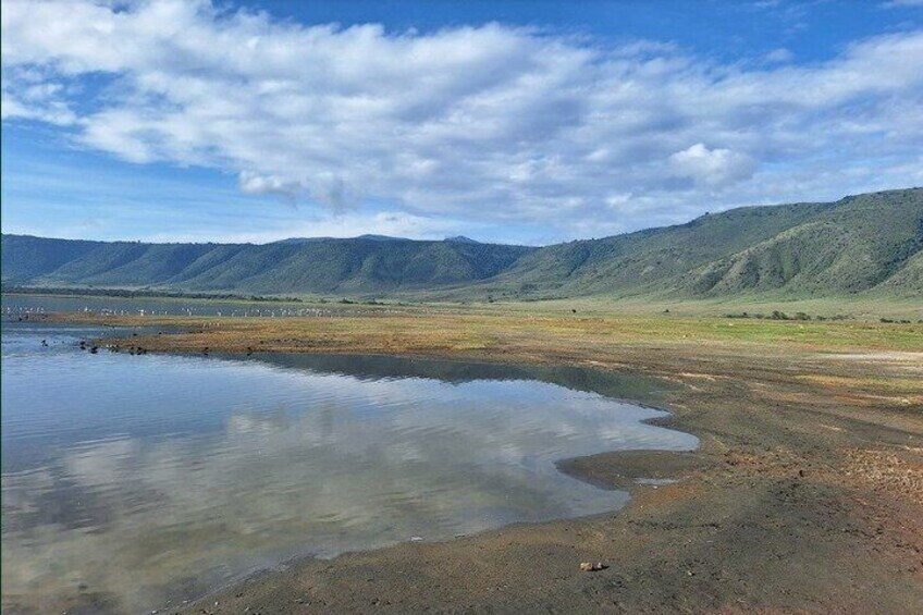 A calm lake with reflections, surrounded by green hills and a clear sky. 1