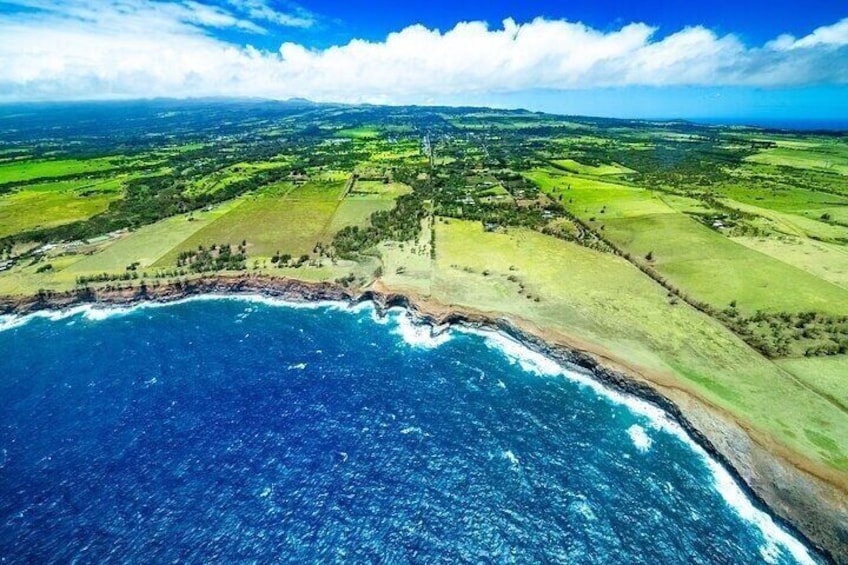An aerial view of a coastal landscape with a clear blue ocean, green fields, and a distant coastline. 2