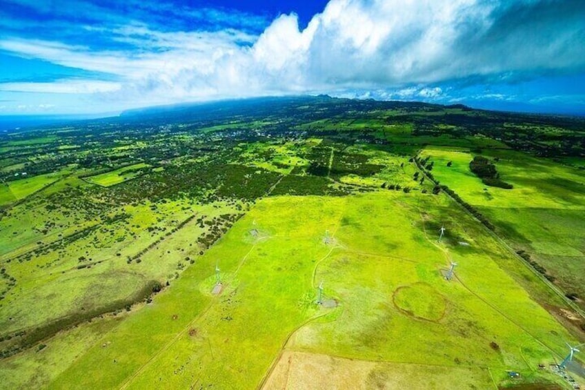 A vast green landscape with fields, a winding road, and distant mountains under a partly cloudy sky. 3