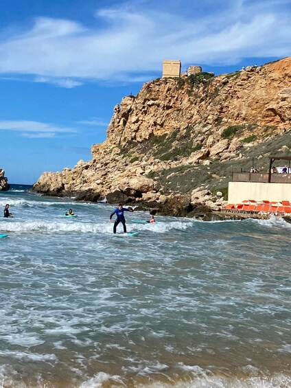 A rocky coastline with surfers and a castle-like structure on a hill. 4