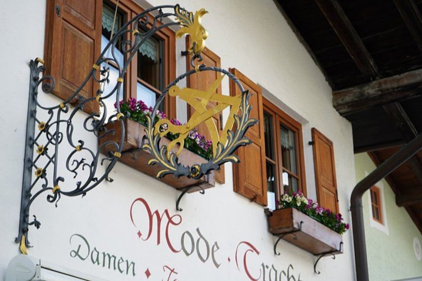A building with wooden shutters, a decorative metal sign, and flower boxes. 2