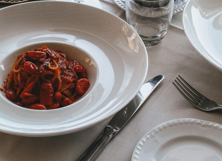 A plate of pasta with a red sauce, a fork, and a knife on a table. 1
