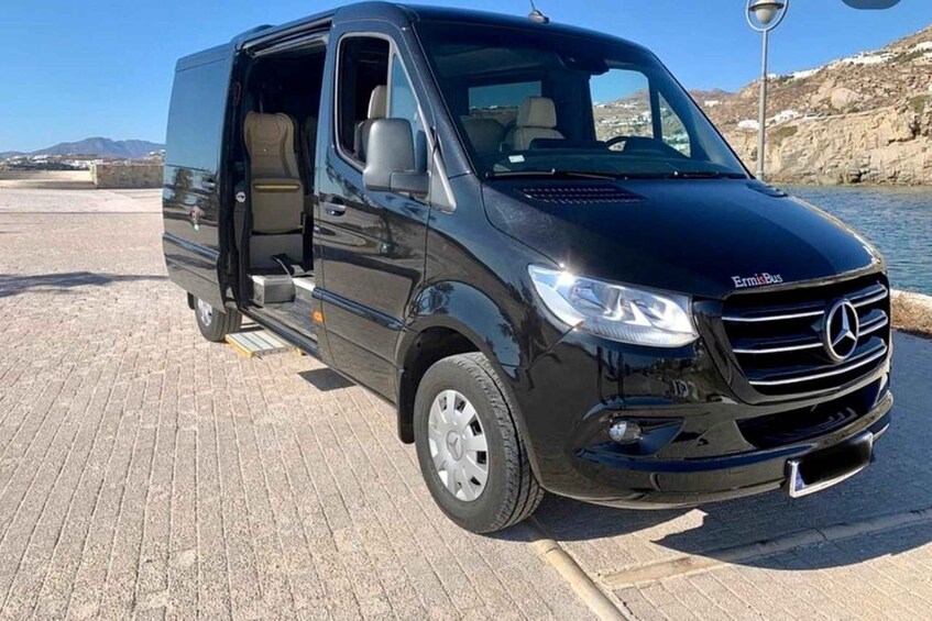 A black Mercedes-Benz Ermis Bus parked by a waterfront with a rocky landscape in the background. 3