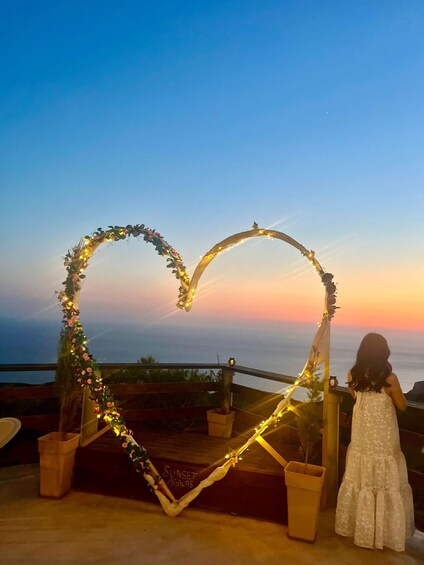 A heart-shaped arch decorated with lights and flowers, overlooking a scenic sunset view. 2