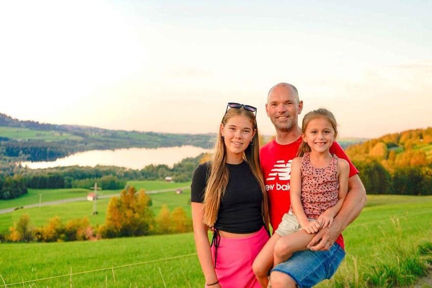 A family of three in a grassy field with a lake and hills in the background. 3