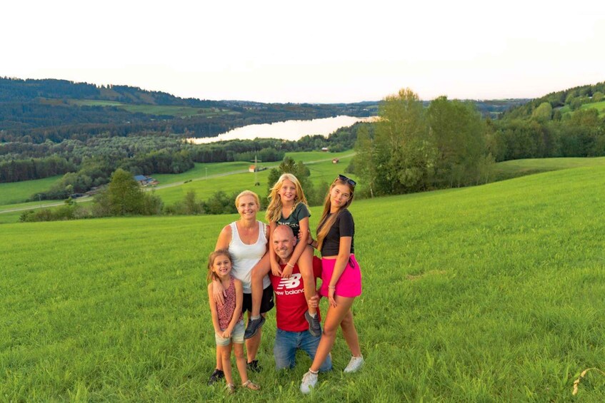 A family of five in a grassy field with a lake and hills in the background. 2