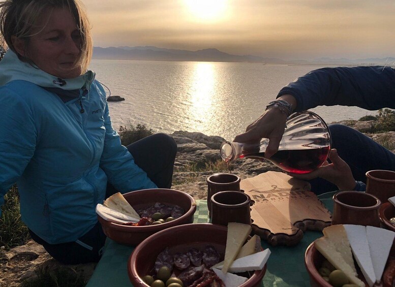 Two people at a table with food and wine, overlooking a body of water and mountains. 1