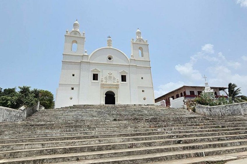 A white church with a bell tower, steps leading up to it, and a clear blue sky. 1