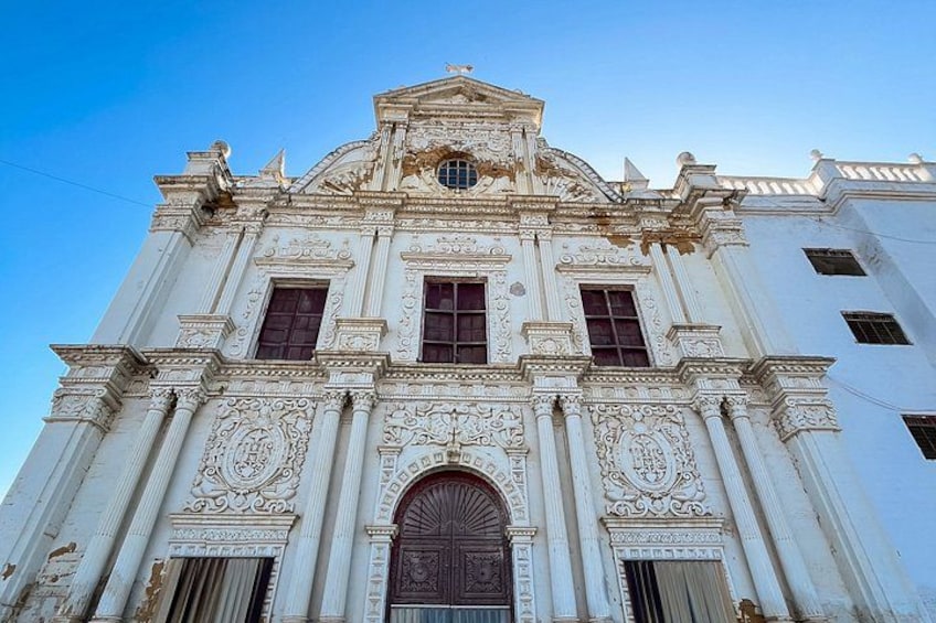 A white building with ornate carvings, a large arched doorway, and a clock tower. 4
