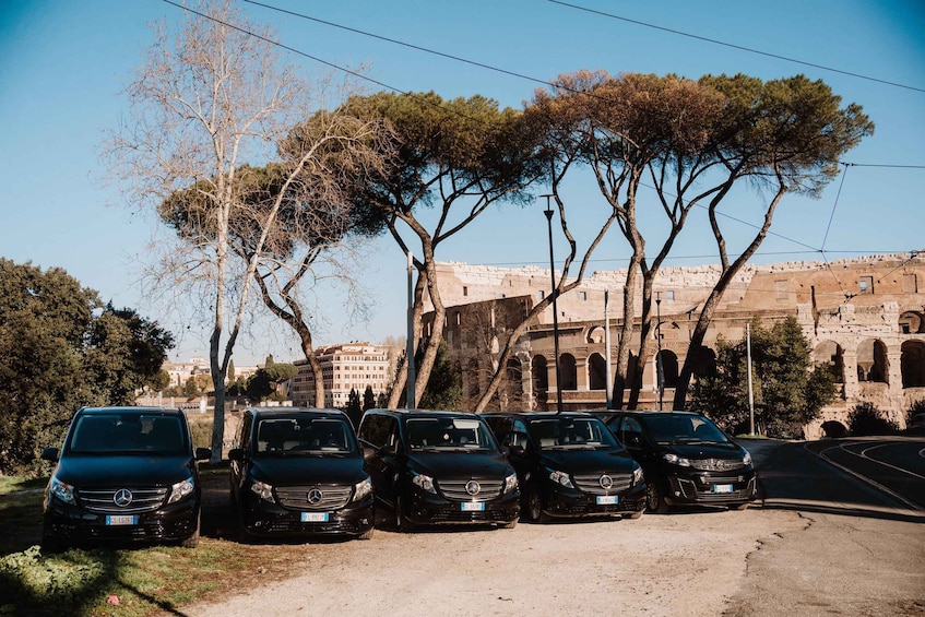 Parked cars, trees, and an ancient building with arches. 2