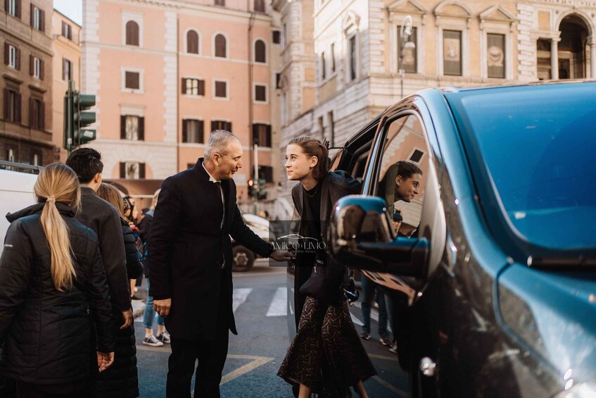 A group of people interacting near a blue car in an urban setting with historic buildings. 4
