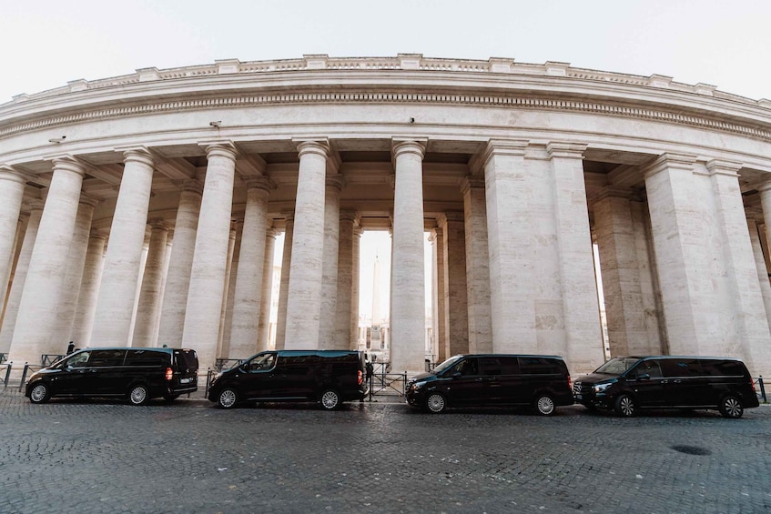 A large neoclassical building with columns and three black vehicles parked in front. 3