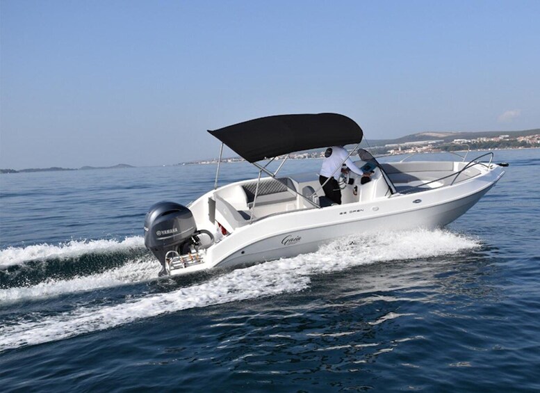 A white motorboat with a Yamaha outboard motor, a person steering, and a clear blue sky in the background. 1