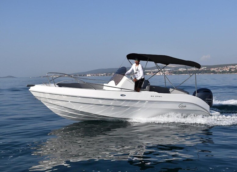 A white motorboat with a canopy, moving on calm water with a coastal landscape in the background. 1